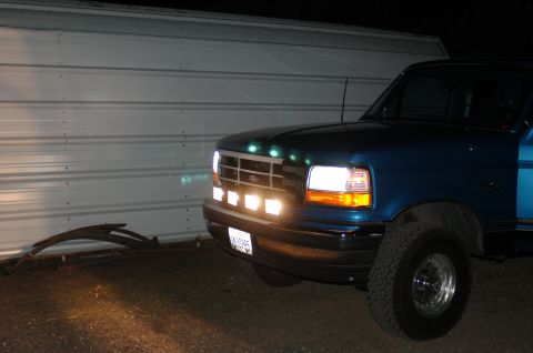 1992 Ford F-150 - A blue 1992 Ford F-150 pickup truck is parked in front of a corrugated metal wall at night.