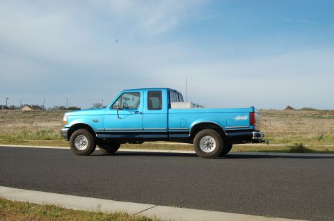 1992 Ford F-150 - This blue 1992 Ford F-150 crew cab pickup truck is shown from the side under a partly cloudy sky.