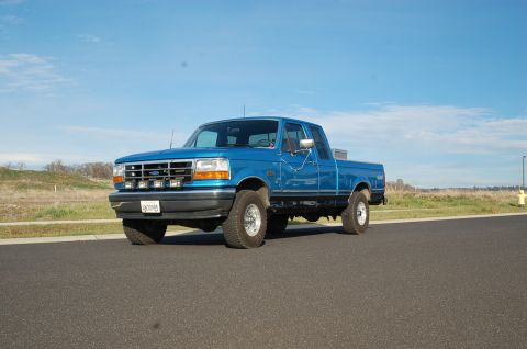 1992 Ford F-150 - A blue 1992 Ford F-150 pickup truck is shown from a three-quarter front view on a clear day.