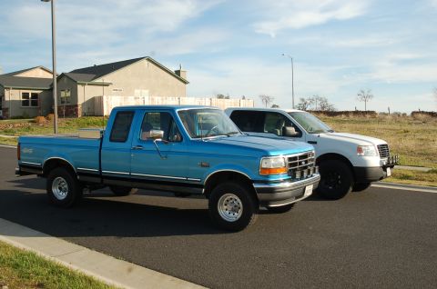 1992 Ford F-150 - A blue 1992 Ford F-150 pickup truck is parked on the street next to a newer white truck.