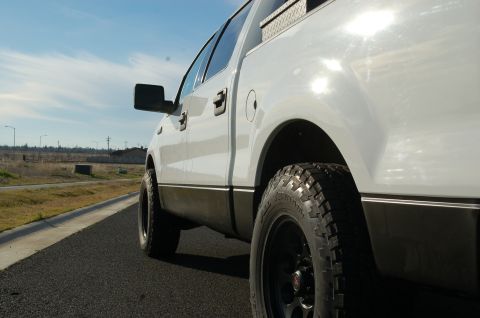1992 Ford F-150 - A white pickup truck is seen from the side, black trim and off-road tires on a sunny day.