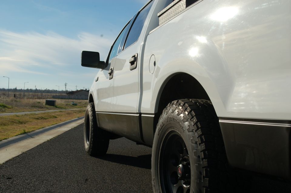 Side view of a white pickup truck with black trim and off-road tires
