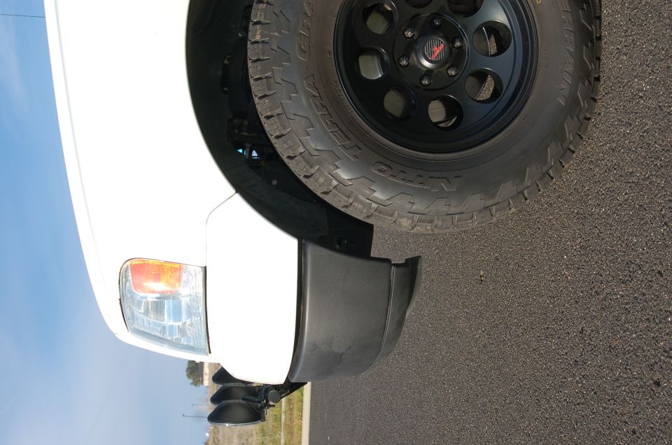 Close-up of a white truck's front fender, headlight, and off-road tire on a black wheel