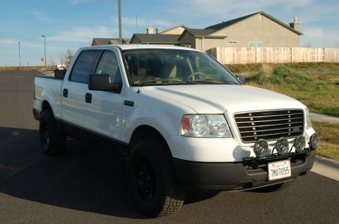 1992 Ford F-150 - This white Ford F-150 pickup truck is shown from a three-quarter front view, with aftermarket lights mounted on the bumper.