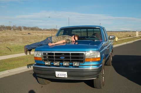 1992 Ford F-150 - A person rests on the hood of a blue 1992 Ford F-150 pickup truck, which features aftermarket fog lights on the front bumper.