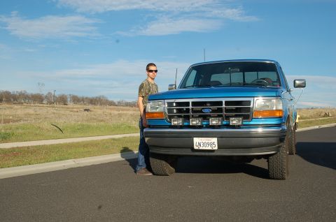 1992 Ford F-150 - A man stands beside a blue Ford F-150 pickup truck on a sunny day.