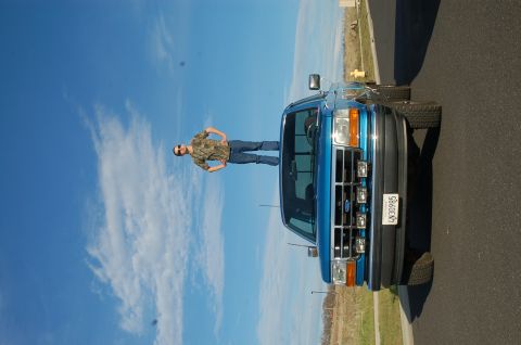 1992 Ford F-150 - A blue 1992 Ford F-150 truck is shown from a 3q-front angle, with a person standing on its roof under a clear blue sky.