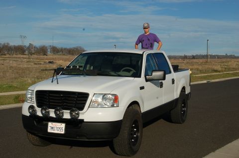 1992 Ford F-150 - A white pickup truck is parked on the side of the road with a person standing on its roof.