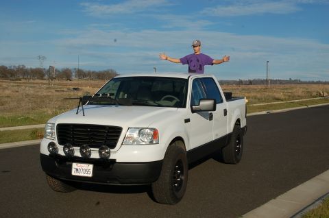 1992 Ford F-150 - A white Ford F-150 pickup truck is shown from the front-right, with a person standing on its roof.