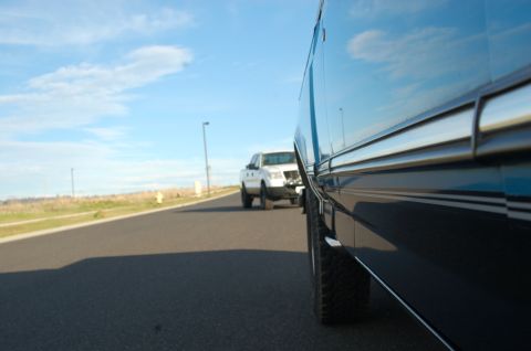 1992 Ford F-150 - A white 1992 Ford F-150 is captured in a side profile as it drives down a road, with another vehicle's reflection visible on the right.