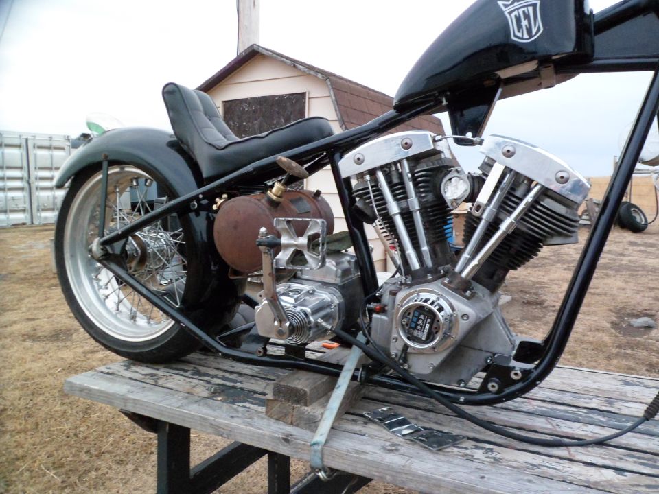 Motorcycle engine and frame on wooden table, black tank with CFL logo