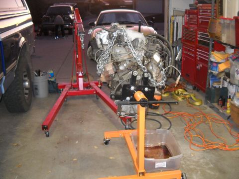 1992 Ford Explorer - An engine is suspended by chains and mounted on an engine stand, with a red engine hoist and a pickup truck in the background.
