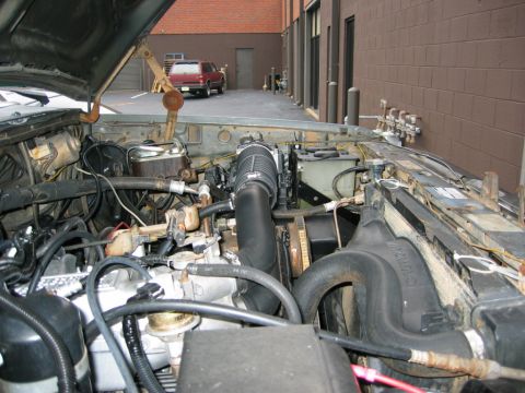 1986 Ford Bronco - The engine bay of a gray SUV is shown with its hood open, while a red SUV is parked in the background.