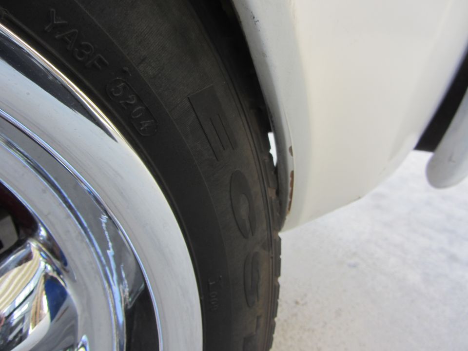 White vehicle's rear wheel well shows rust and damage near the tire with chrome trim