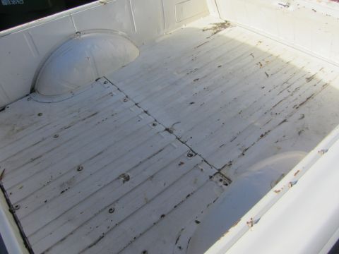 1964 Ford Ranchero - The interior of a white pickup truck bed shows wear and tear on its ribbed floor.