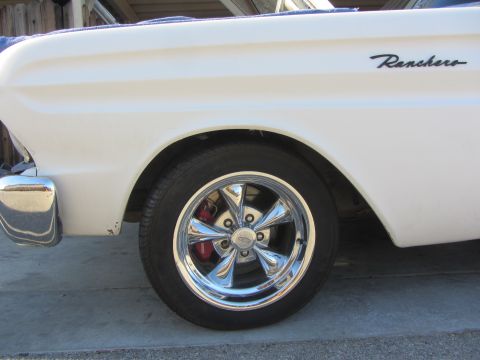 1964 Ford Ranchero - Close-up of a white 1964 Ford Ranchero's side profile, highlighting the fender and a chrome wheel with red brake calipers.