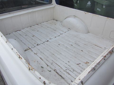1964 Ford Ranchero - The rear of a white pickup truck shows a worn bed with wooden planks and signs of rust along the sides.