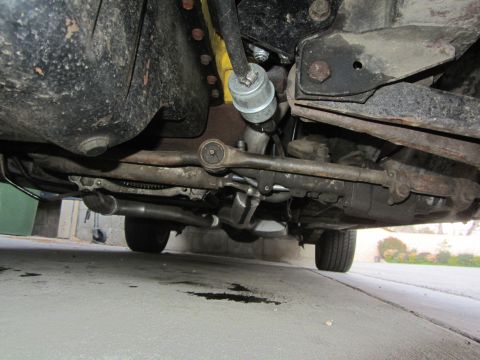 1964 Ford Ranchero - The undercarriage of a vehicle is shown, with visible suspension components and exhaust pipes. There are oil stains on the concrete below.