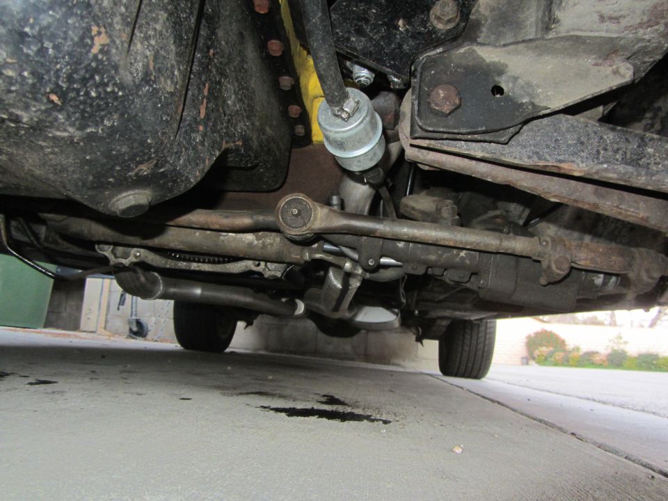 Underside view of a vehicle's suspension and exhaust system. Oil stains on the ground