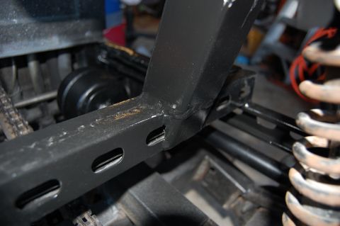2010 Kawasaki BAYOU 220 - Close-up view of a black metal frame section with oval cutouts, adjacent to a coil spring and mechanical components.