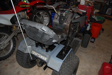 2010 Kawasaki BAYOU 220 - A Craftsman riding mower is shown in a garage, with a dirt bike visible to its left.