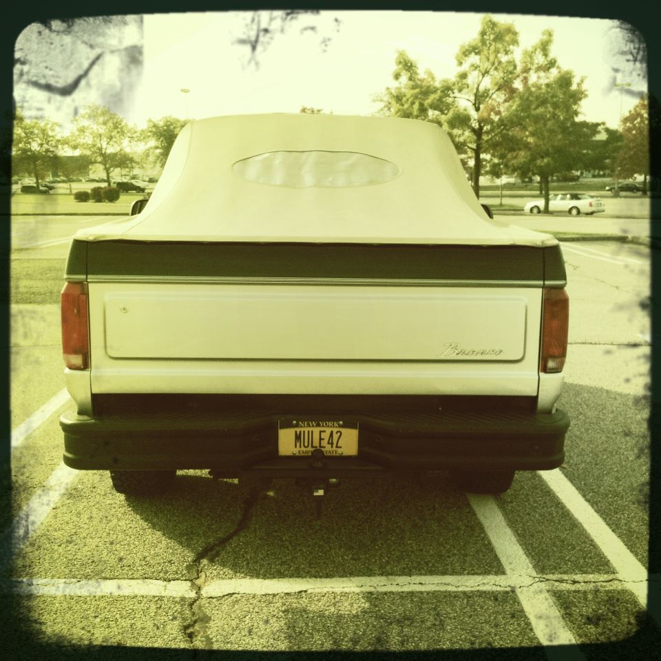 White Ford Bronco with a tan soft top parked in a lot, rear view