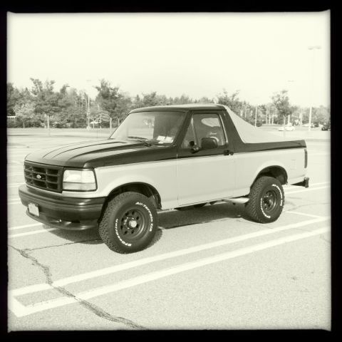 1992 Ford Bronco - This 1992 Ford Bronco is parked in a lot with trees in the background.