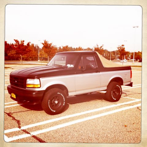 1992 Ford Bronco - This two-tone Ford Bronco is parked in a lot with trees in the background.