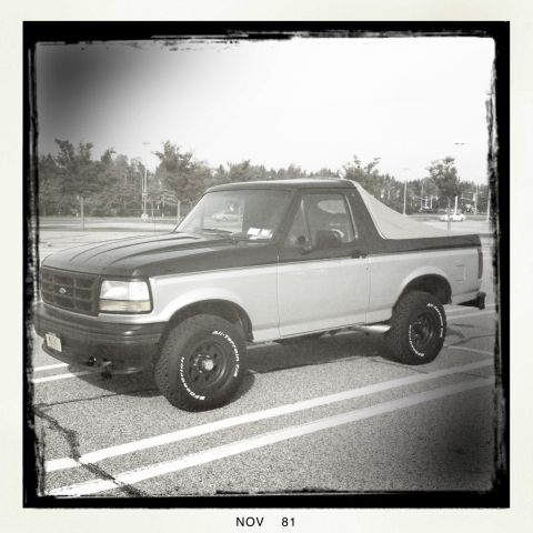1992 Ford Bronco - A two-tone 1992 Ford Bronco is parked in a lot, showing its side profile and removable top.
