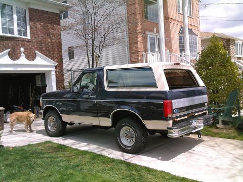 1992 Ford Bronco - A two-door Ford Bronco with a tan removable top is parked in a suburban driveway.