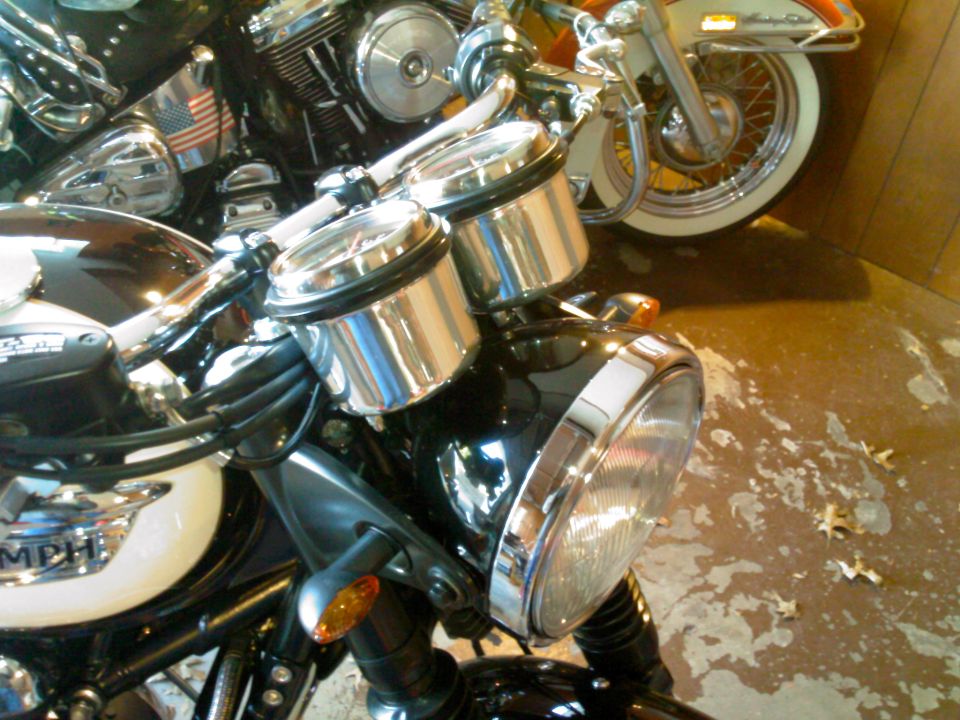 Black motorcycle with twin chrome gauges and round headlight, other bikes behind on concrete floor