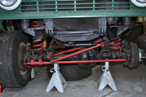 1974 Ford Bronco - Front suspension and undercarriage of a green 1974 Ford Bronco, red shocks and springs, supported by jack stands.