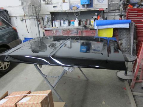 1987 Dodge 1500 - A black vehicle hood is propped up on a stand in a workshop, likely undergoing repairs or detailing.