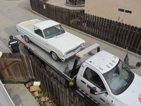 1964 Ford Ranchero - A white 1964 Ford Ranchero is winched onto a flatbed tow truck by a worker.
