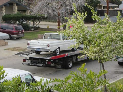 1964 Ford Ranchero - A white 1960s Ford Ranchero is loaded onto a tow truck, with a red minivan and another vehicle visible in the background.