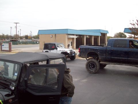 1989 Ford Bronco - Multiple lifted off-road vehicles are parked outside a building.
