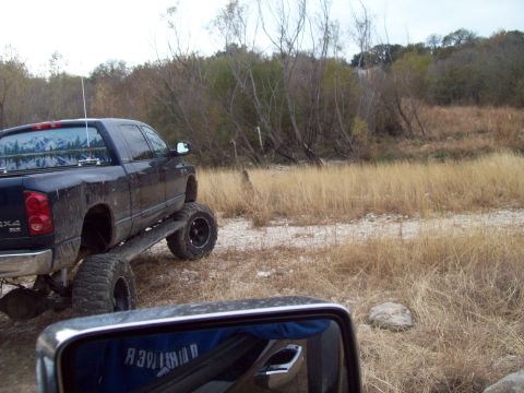 1989 Ford Bronco - A lifted pickup truck is parked off-road, with a reflection of a person in the side mirror.
