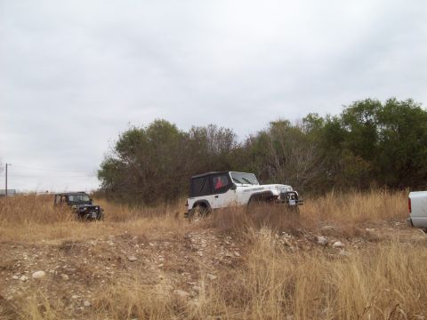 1989 Ford Bronco - Two Jeeps are parked in a field of dry grass under an overcast sky.