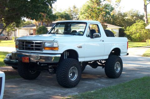 1995 Ford Bronco - White full-size Ford Bronco with a suspension lift, oversized mud tires and aftermarket wheels parked in a yard.