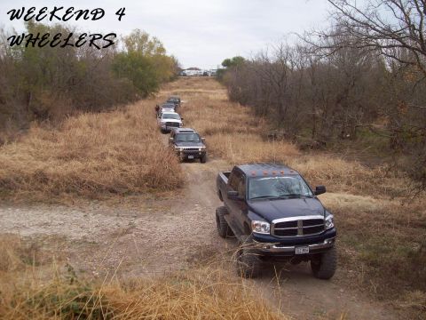 1989 Ford Bronco - Several off-road vehicles drive in a convoy along a dry, grassy trail under an overcast sky.