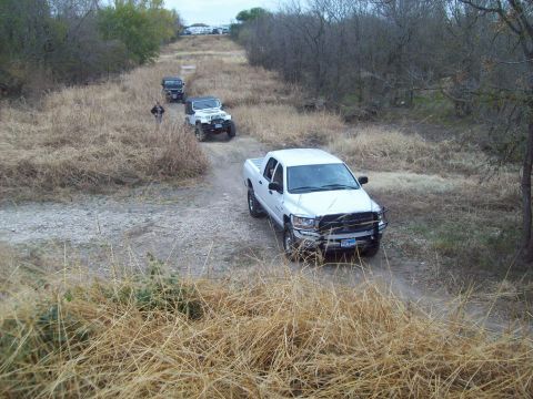 1989 Ford Bronco - Several off-road vehicles, including a white pickup and Jeeps, navigate a dirt path.