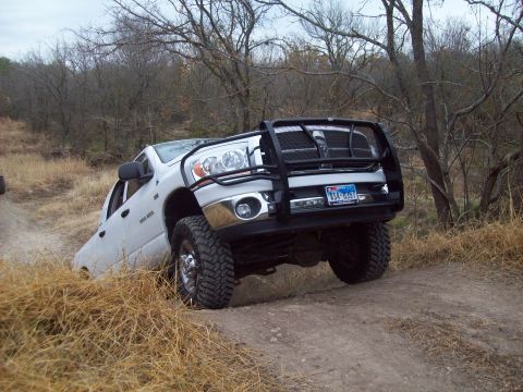 1989 Ford Bronco - A white pickup truck navigates a rough dirt trail, its front tires angled on the uneven terrain.