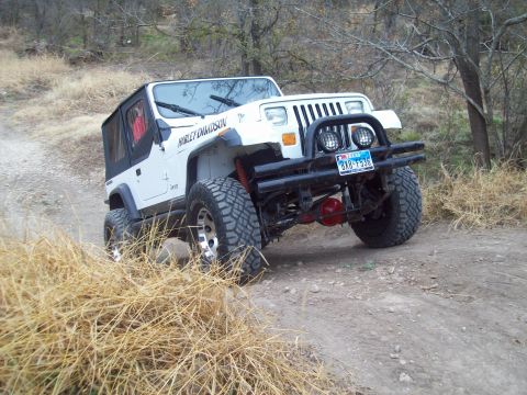 1989 Ford Bronco - A white Jeep Wrangler is shown on a dirt trail with dry grass in the foreground.
