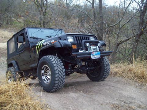 1989 Ford Bronco - Off-road Jeep Wrangler with Monster Energy decals navigating a wooded trail.