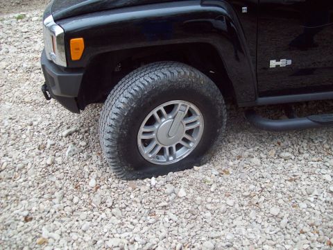 1989 Ford Bronco - A black SUV sits with a flat tire on a gravel surface.
