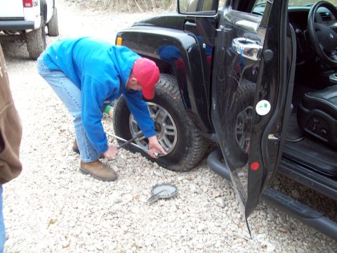 1989 Ford Bronco - A person works to change a flat tire on a black SUV, with another vehicle visible in the background.