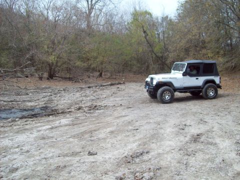1989 Ford Bronco - White Jeep Wrangler sits on a muddy, wooded trail.