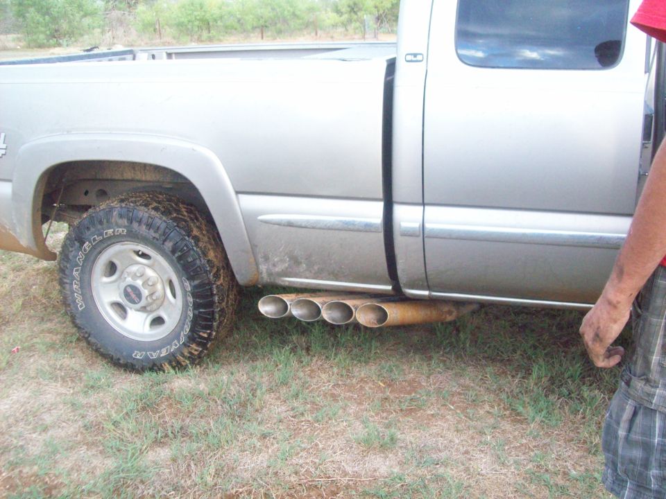 Silver pickup truck side view, showing quad exhaust pipes and muddy tires