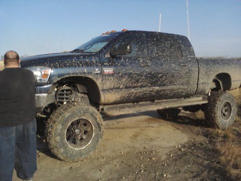 1989 Ford Bronco - A lifted, mud-splattered Dodge Ram 3500 pickup truck sits off-road under a clear sky.