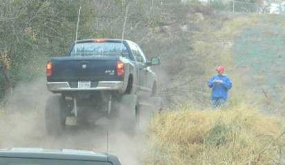 1989 Ford Bronco - A lifted black pickup truck navigates a dusty, off-road path with a person watching.